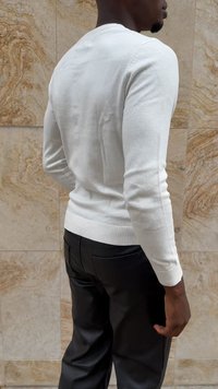 Suéter blanco de punto con mangas largas, dobladillo acanalado y silueta ajustada, combinado con pantalones de cuero negros, visto desde la parte posterior.