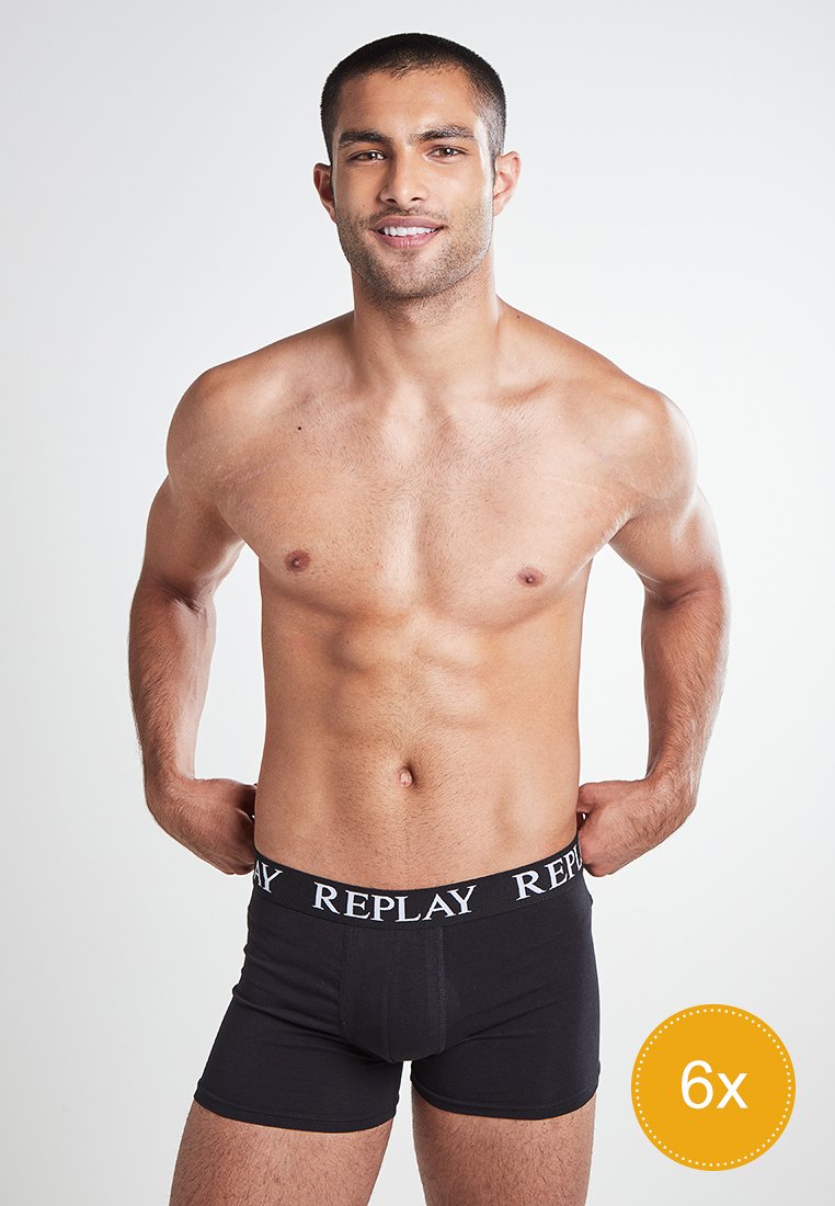 Schwarze Baumwoll-Boxershorts mit einem Logo-Gummibund, entworfen für Komfort, präsentiert von einem Modell vor einem neutralen Hintergrund.