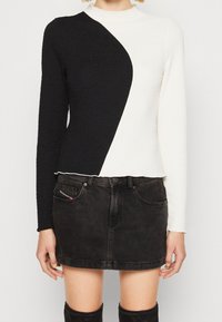 Langärmliger Rollkragenpullover mit einem strukturierten Design, diagonal in schwarze und weiße Paneele unterteilt. Getragen mit einem eng anliegenden schwarzen Jeansrock.
