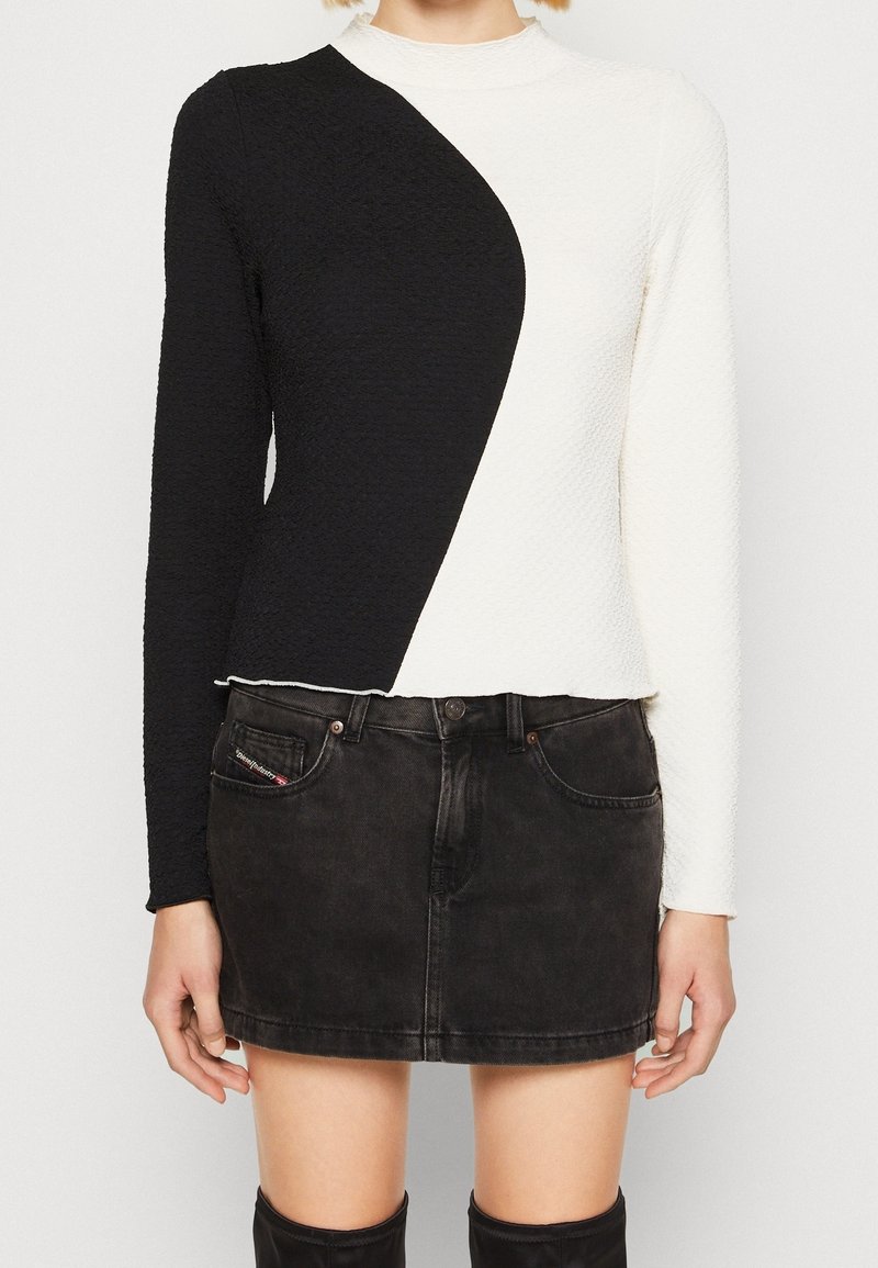 Langärmliger Rollkragenpullover mit einem strukturierten Design, diagonal in schwarze und weiße Paneele unterteilt. Getragen mit einem eng anliegenden schwarzen Jeansrock.