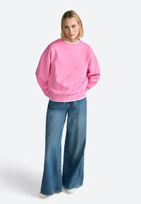 Sweatshirt rose avec col rond et poignets côtelés, associé à un jean bleu à jambe large. Tissu décontracté et coupe détendue.
