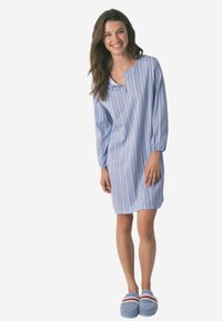 Camicia da notte a righe blu chiaro in tessuto morbido, con maniche lunghe, collo tondo e un parziale abbottonatura; abbinata a pantofole blu.