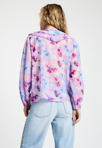 Florale Kapuzenjacke in Pastelltönen von Rosa, Lila und Blau. Leichter Stoff mit langen Ärmeln und elastischen Bündchen. Legerer Schnitt.