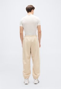 Light gray short-sleeve shirt with "TECHFIT" label, paired with loose beige sweatpants and white sneakers, viewed from the back.