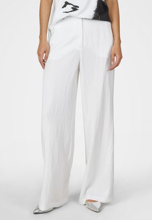 Person wearing white wide-leg pants, metallic pointed shoes, and a white and black graphic t-shirt against a plain background.