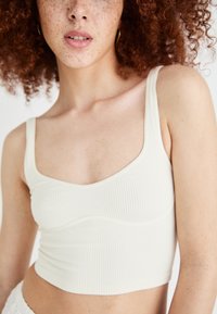 Ribbed white cropped tank top with wide shoulder straps and rounded neckline, featuring a fitted shape and subtle seam detailing.
