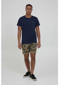 Temno modra bombažna majica v kombinaciji s kaki kratkimi hlačami z zelenim listnim vzorcem. Črni športni copati dopolnjujejo videz. Preprost dizajn in sproščen kroj.