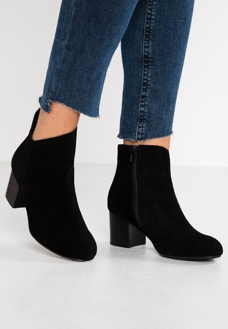 Stivaletti alla caviglia in suede nero con tacco quadrato, taglio curvo alla caviglia e dettaglio con cerniera laterale; superficie strutturata e colore uniforme.