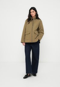 Κυπαρισσί πράσινο μπουφάν με ραφές, με ψηλό γιακά, φερμουάρ μπροστά και δύο μεγάλες τσέπες. Συνδυάζεται με φαρδιά σκούρα τζιν παντελόνια.