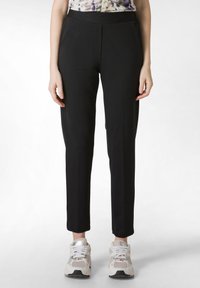 Zwarte fitted broek met een gladde textuur, voorzien van zijzakken en een op maat gemaakte pasvorm, gecombineerd met lichtgekleurde sportschoenen.