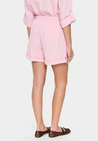 Shorts in cotone rosa chiaro con cintura elastica, orli arrotolati e tasche laterali, che mostrano una vestibilità comoda e una texture liscia.
