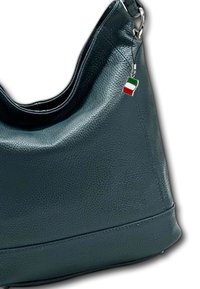 Sac à main en cuir texturé vert avec une forme courbée et un accent en métal argenté. Il comporte un petit charm représentant le drapeau italien sur la bandoulière.