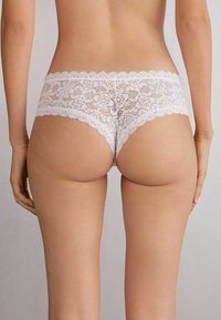 Witte kanten hipster onderbroek met bloemenpatroon, scalloped randen en een elastische tailleband. Zachte textuur met een semi-transparante afwerking.