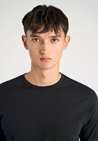 Maglia nera a maniche lunghe con scollo rotondo e un logo ricamato in modo sottile sul petto, realizzata in un tessuto liscio e leggero.