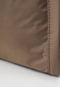 Bruine stoffen tas met een gladde textuur, featuring een tonale geborduurde logo. Het ontwerp is eenvoudig zonder zichtbare hardware of extra patronen.