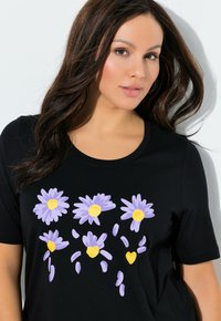 Czarny t-shirt z krótkim rękawem z kwiatowym wzorem pięciu fioletowych stokrotek z żółtymi środkami, na tle gładkiej tekstury materiału.
