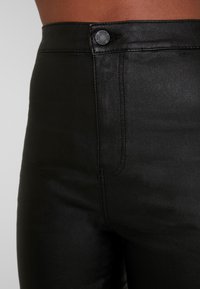 Svart hög midja byxor med en slät textur, med knappstängning och subtila sömnadsdetaljer längs sidfickorna.