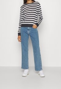 Gestreifter Pullover in marineblau und weiß aus Baumwolle, kombiniert mit hochgeschnittenen, hellblauen Jeans. Das Model trägt weiße Sneakers.
