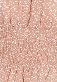 Tissu rose avec un motif abstrait blanc, featuring un détail smocké pour plus d'élasticité. Texture douce, design froncé à l'ourlet.