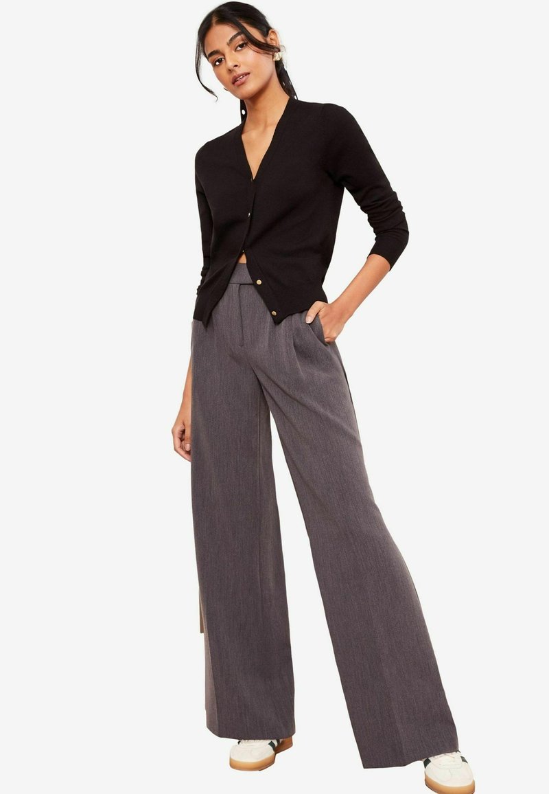 Cardigan negru cu decolteu în formă de V și mâneci trei sferturi, asortat cu pantaloni gri cu picioare largi, având o textură subtilă și pliuri.