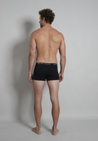 Caleçons boxers noirs en tissu doux avec une taille élastique affichant le logo "TOM TAILOR". Le modèle est montré de dos.
