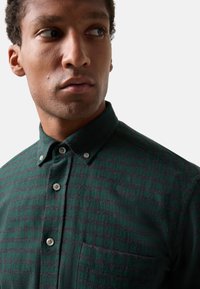 Donkergroene geruite overhemd gemaakt van textuurstof, met een kraag met knopen, grijze accenten en een enkele borstzak.