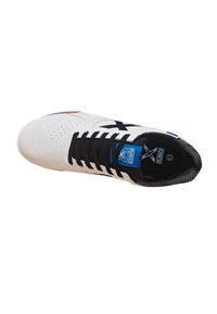 Zapato de cuero blanco con cordones negros, superficie texturizada y detalles perforados. Presenta una etiqueta azul y un forro de malla negra.