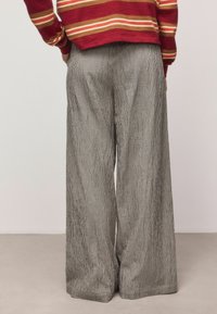 Wide-leg trousers in black and white check pattern, featuring a smooth texture and tailored fit, paired with a red striped sweater.