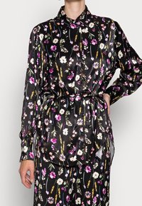 Black satin shirt with long sleeves, floral print in pink, white, and green. Features a collar and a tie belt at the waist.