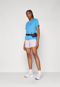 Camiseta atlética azul, pantalones cortos rosas claros, cinturón de running negro, calcetines blancos y zapatillas de correr rosas con acentos morados. Tejido suave, ajuste relajado.