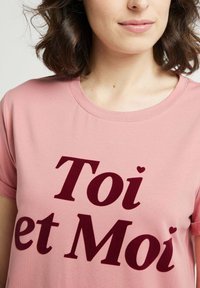 T-shirt rose clair avec un grand texte en bordeaux foncé indiquant "Toi et Moi", agrémenté de petits cœurs sur les lettres. Tissu doux, encolure ronde.