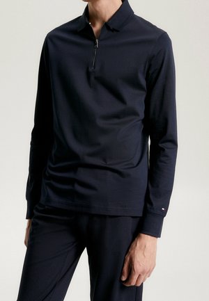 Navy long-sleeve polo shirt with a quarter zip, smooth fabric, flat collar, and subtle logo accent on the sleeve. Tailored fit.