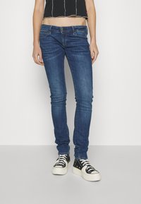 Jeans ajustados en denim azul oscuro con un acabado deslavado, que cuentan con un cierre de cremallera, cinco bolsillos y un sutil detalle de costura a lo largo de la cinturilla.