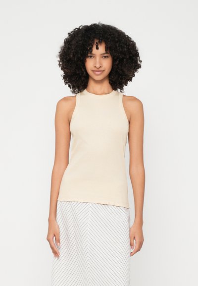 Top sin mangas de color beige claro con textura acanalada y un cuello alto, combinado con una falda que presenta finas rayas diagonales en blanco y marino.