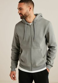 Grauer Reißverschluss-Hoodie mit Kängurutasche, verstellbarem Kordelzug und gerippten Bündchen. Das Material wirkt weich mit einer glatten Textur.
