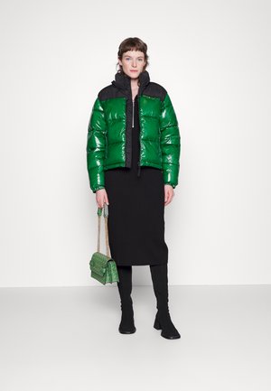 Casaco puffer verde e brilhante com detalhes pretos, fecho de zip e gola alta; combinado com uma saia preta em malha e botas altas pretas; bolsa verde.