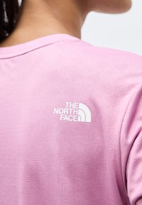 Κοντινή εικόνα του άνω μέρους της πλάτης ενός ατόμου που φοράει ροζ υφασμάτινο πουκάμισο με λευκό λογότυπο The North Face στον δεξί ώμο.