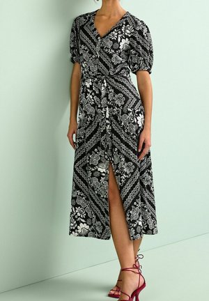 Schwarz-weißes Maxikleid mit Blumenmuster, V-Ausschnitt, Puffärmeln und hohem Beinschlitz. Kombiniert mit bordeauxroten Riemchenabsätzen.