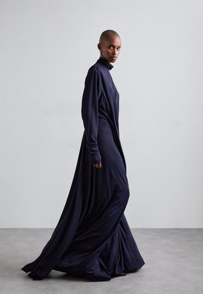 Long, flowing navy dress made of soft fabric with a high neck and long sleeves. Features draping and a sleek silhouette.