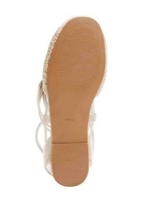 Beige sandaalin pohja, jossa on teksturoitu kumi, hieman kohotettu korko, pyöreä muoto ja kudotut yksityiskohdat reunoilla. Brändin nimi painettuna pohjaan.