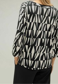 Blusa astratta in bianco e nero con maniche a tre quarti, scollatura rotonda e una morbida texture del tessuto. Abbinata a pantaloni neri.