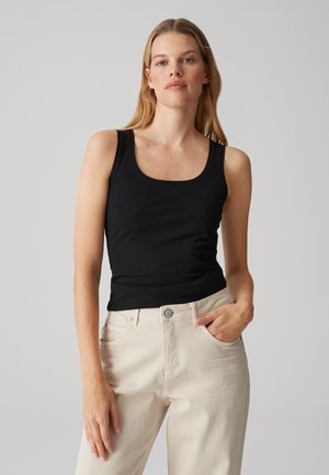 Débardeur noir sans manches en tissu doux, avec un col en scoop et une coupe ajustée, associé à un pantalon taille haute beige clair.
