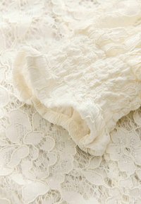 Blonde stof med indviklede blomsterdesigns i off-white, parret med en samlet, struktureret sektion, der skaber et blødt, lagdelt udseende.