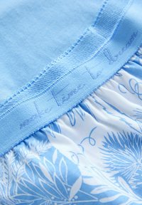 Hellblaue Bekleidung mit einem strukturierten, einfarbigen oberen Abschnitt und einem floral bedruckten unteren Abschnitt. Enthält gestickten Text "Nimm dir Zeit zum Träumen" auf dem Bund.