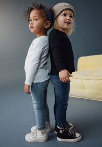 To børn står ryg mod ryg. Den ene har en hvid langærmet trøje, lyseblå jeans og hvide sneakers på. Den anden har en sort trøje, mørke jeans og sorte sneakers på.