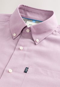 Cămașă mov deschis cu nasturi, guler clasic, nasturi albi, buzunar la piept și o etichetă mică cu brand pe buzunar.
