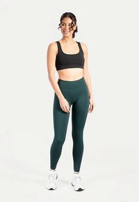 Zwarte sport-bh en bosgroene legging met hoge taille gemaakt van rekbaar materiaal, ontworpen voor comfort en actieve draagbaarheid. Witte sneakers maken de look compleet.