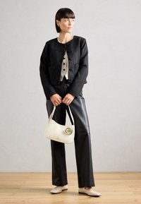Chaqueta negra corta con botones, blusa rayada beige, pantalones de cuero negros, bolso blanco con un detalle de rosa y bailarinas beige.