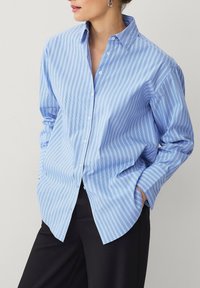Helle blaue Button-Down-Bluse mit vertikalen weißen Streifen. Verfügt über einen Kragen, lange Ärmel und eine lockere Passform. Glattes Baumwollgewebe.