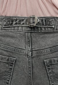 Κοντινό πλάνο του πίσω μέρους γκρι τζιν με ρυθμιζόμενο λουράκι με αγκράφα και φθαρμένο ροζ πουκάμισο μαζεμένο μέσα.